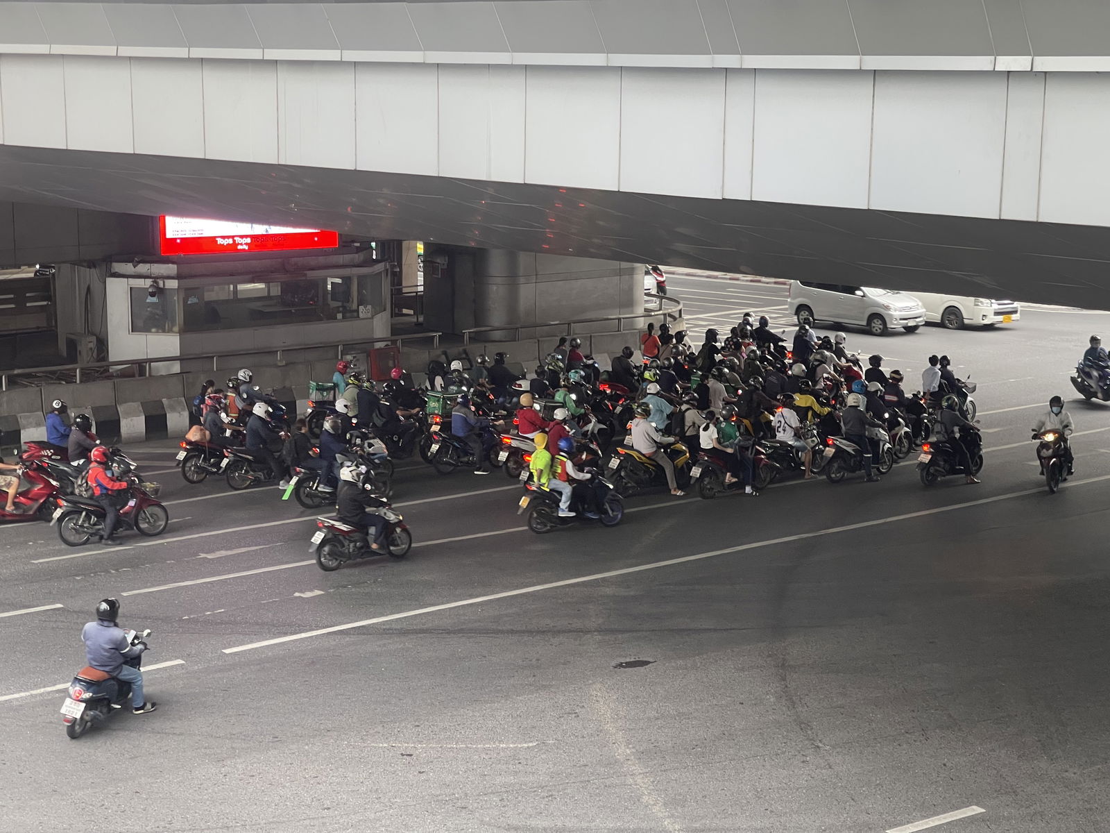 A large number of scooters congregate under a bridge