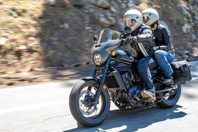 A cruiser motorcycle with a rider and pillion on a sunny day