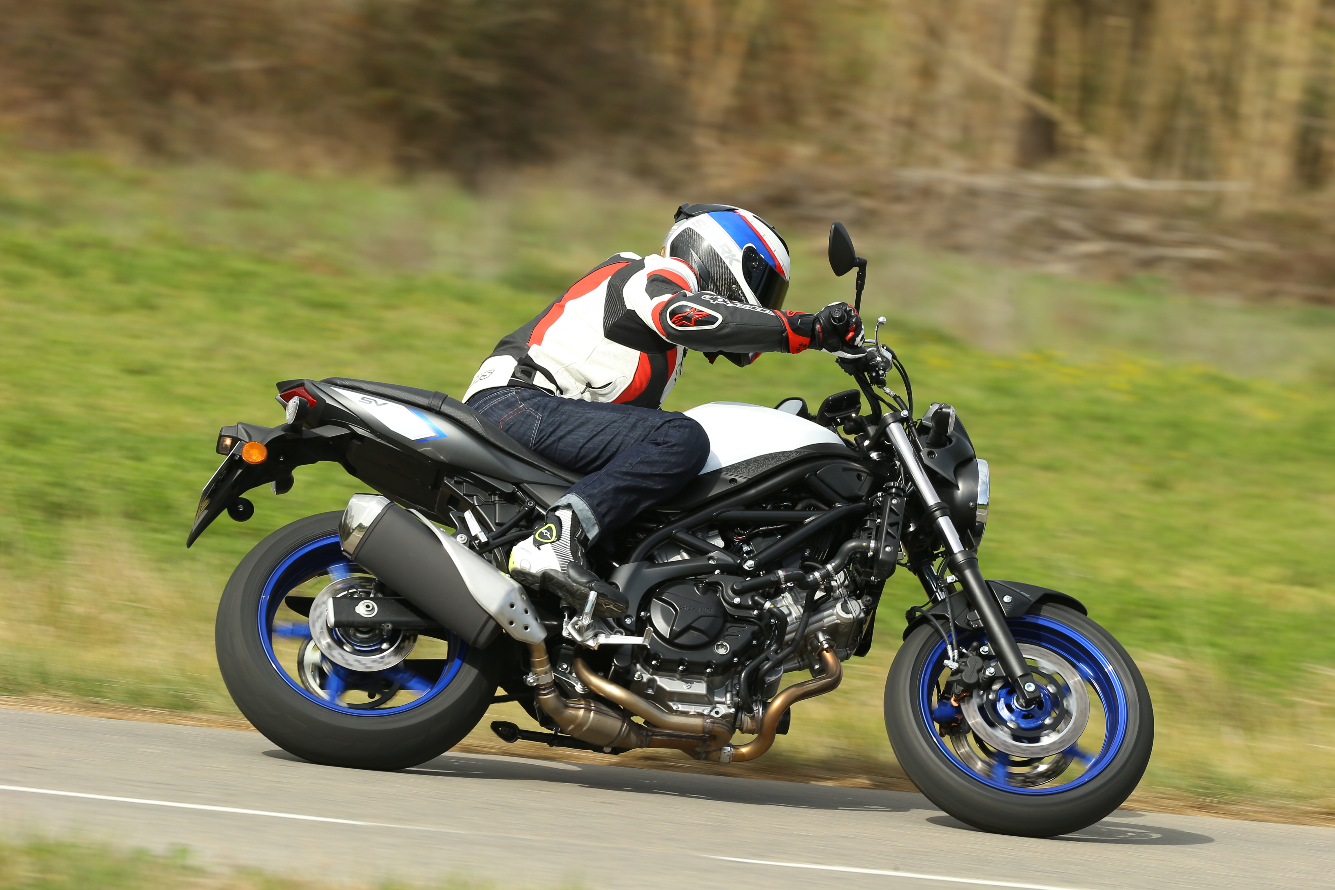 A black and white 2016 Suzuki SV650 being ridden down a country road
