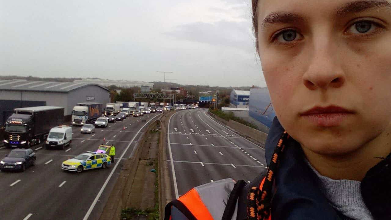 Just Stop Oil protester on M25 gantry, the road is closed behind her. - Just Stop Oil