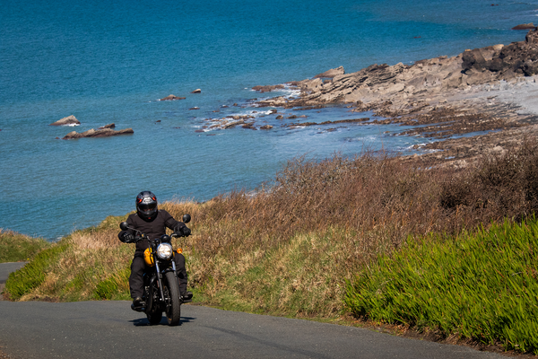 Royal Enfield passing along coastal road with sea in background.