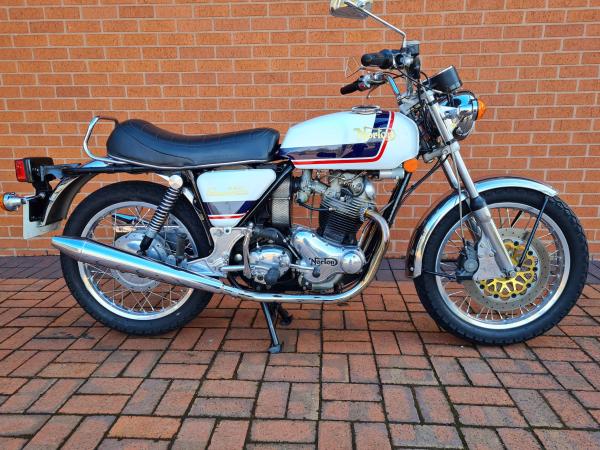 Norton Commando in front of a brown brick wall.