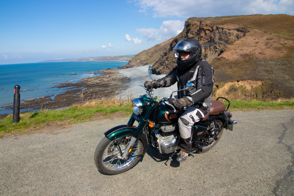 Royal Enfield passing along coastal road with sea in background.