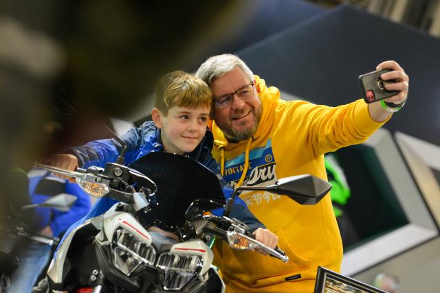 Older man and youner boy having a selfie together whilst the boy is sat on a motorcycle
