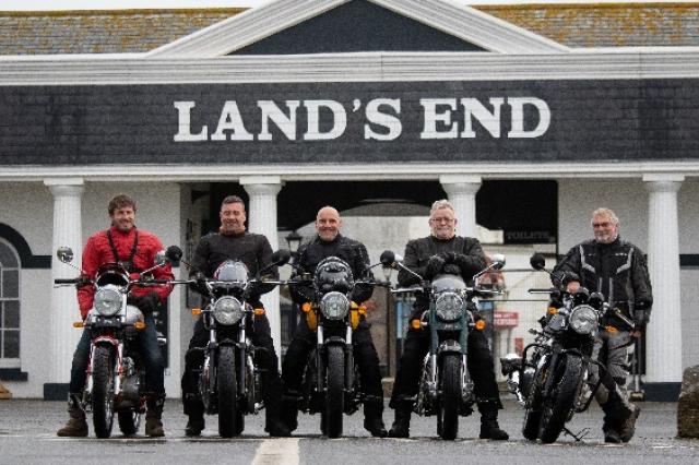 Royal Enfield riders sat stationary on bikes in front of 'Land's End' sign.