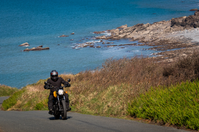 Royal Enfield passing along coastal road with sea in background.