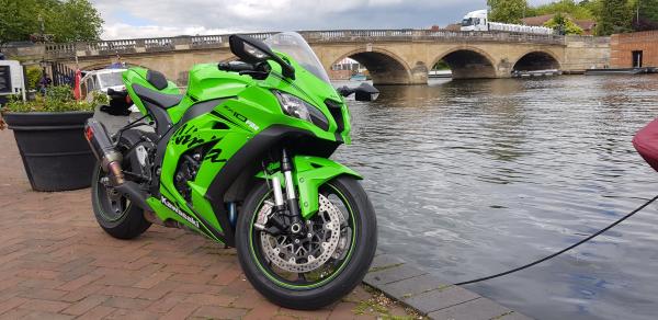 A green and black 2019 Kawasaki Ninja ZX-10RR parked alongside a river with a bridge in the background