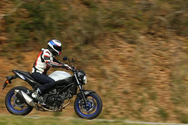 A black and white 2016 Suzuki SV650 motorbike being ridden down a country road