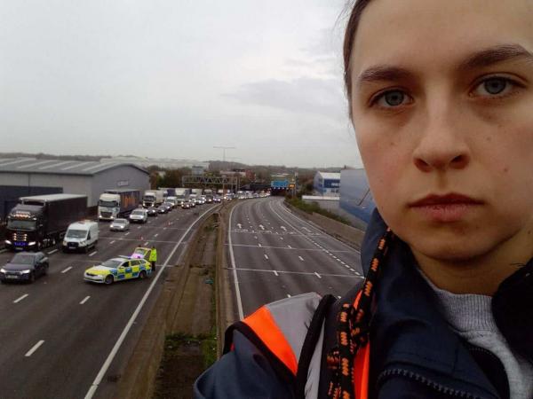 Just Stop Oil protester on M25 gantry, the road is closed behind her. - Just Stop Oil