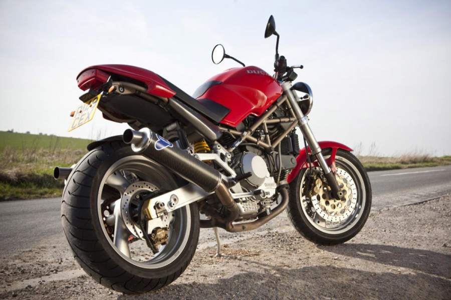 A red and black 1993 Ducati Monster M900 parked by the side of a rural road