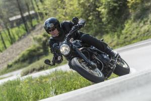 A black Ducati Scrambler Café Racer 2017 being ridden on a rural road